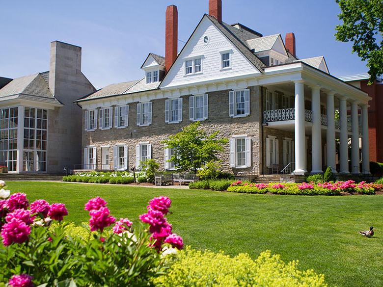 The well kept grounds at the Hintz Family Alumni Center at Penn State's University Park campus with flowers in the foreground an a mallard duck on the lawn